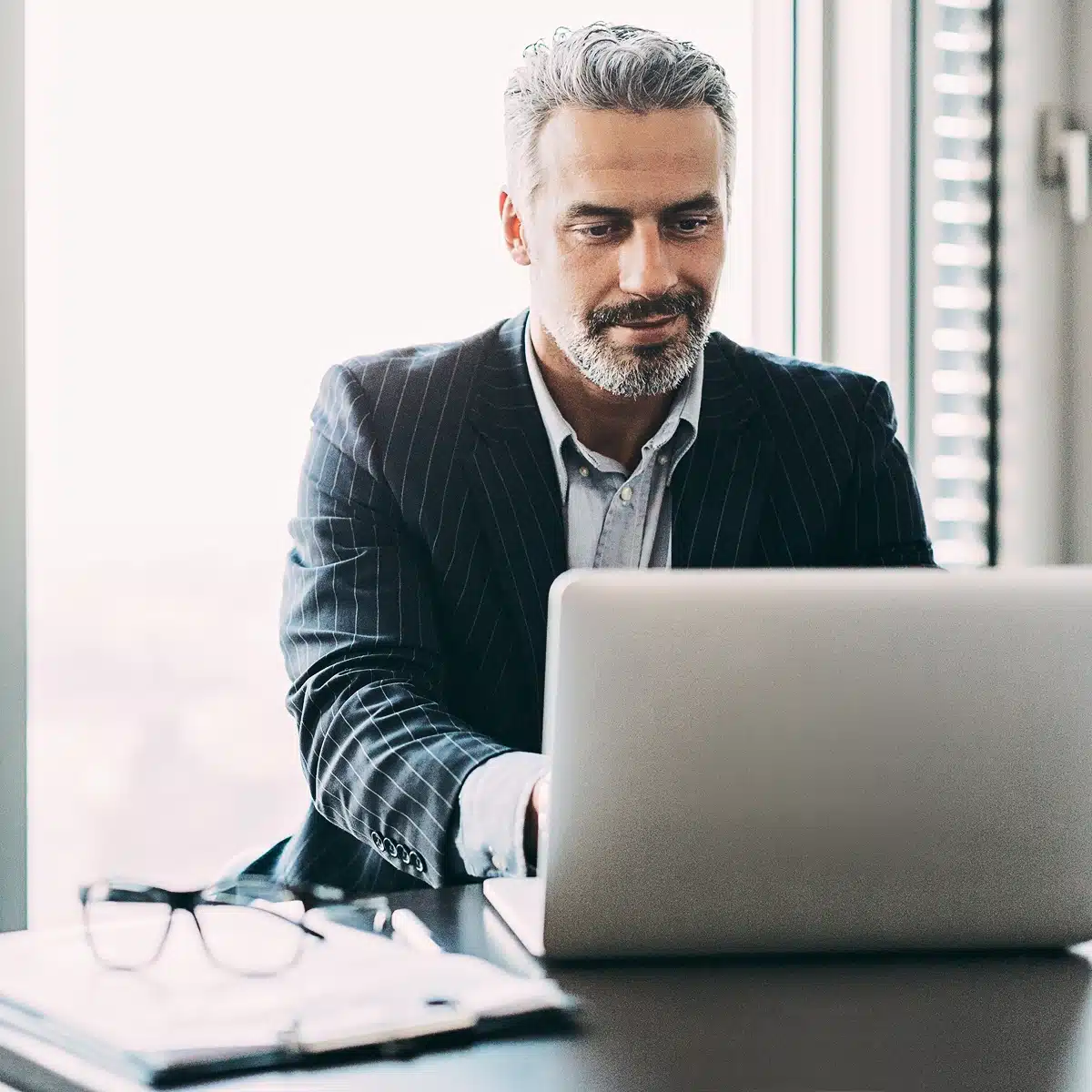 Chief Information Security Officer (CISO) working on a laptop in a modern office. A cybersecurity executive in a pinstripe suit focuses on digital risk management, executive protection, and corporate cybersecurity strategy.
