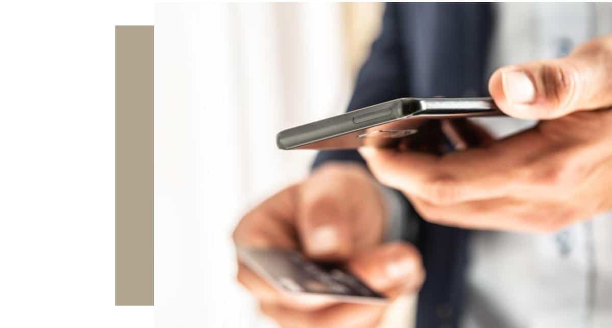 A person holds a black smartphone horizontally in their right hand, with their left hand holding a credit card blurred in the foreground, illustrating personal data security threats and the dangers of accessible personal data.